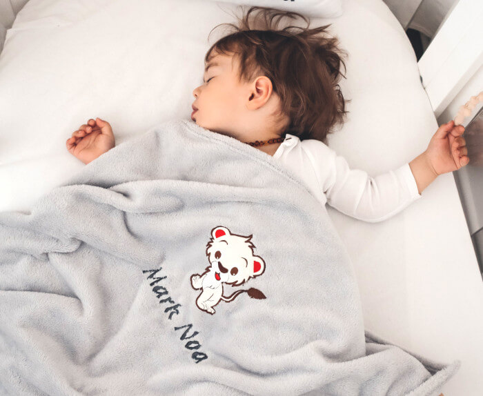 Kleiner Junge, der mit seiner personalisierten grauen Decke bedeckt schläft