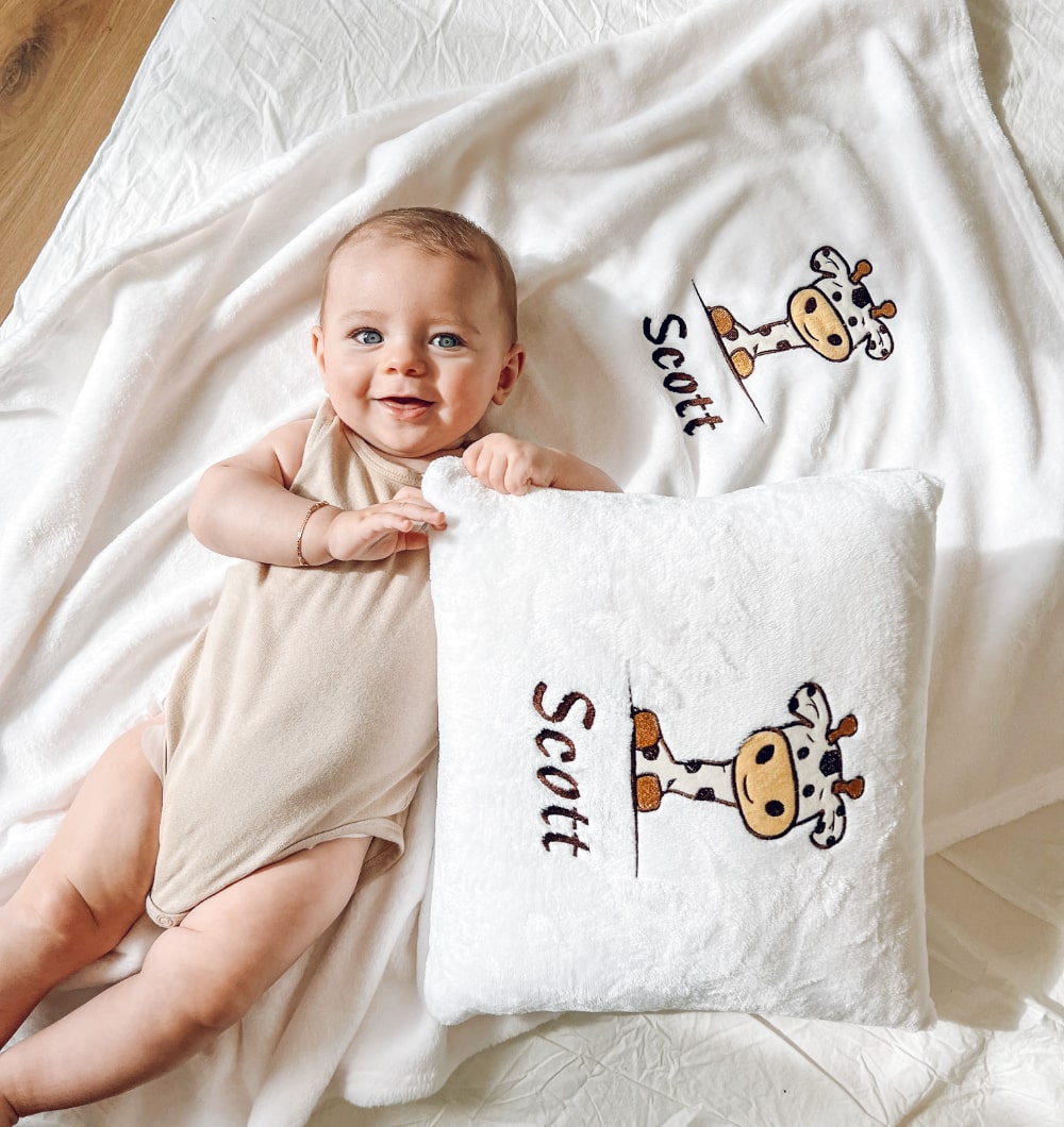 Schattige babyjongen rust vredig op zijn bed, knus met een zachte en gezellige gepersonaliseerde kussen en deken, aangepast met zijn naam en een charmant ontwerp.