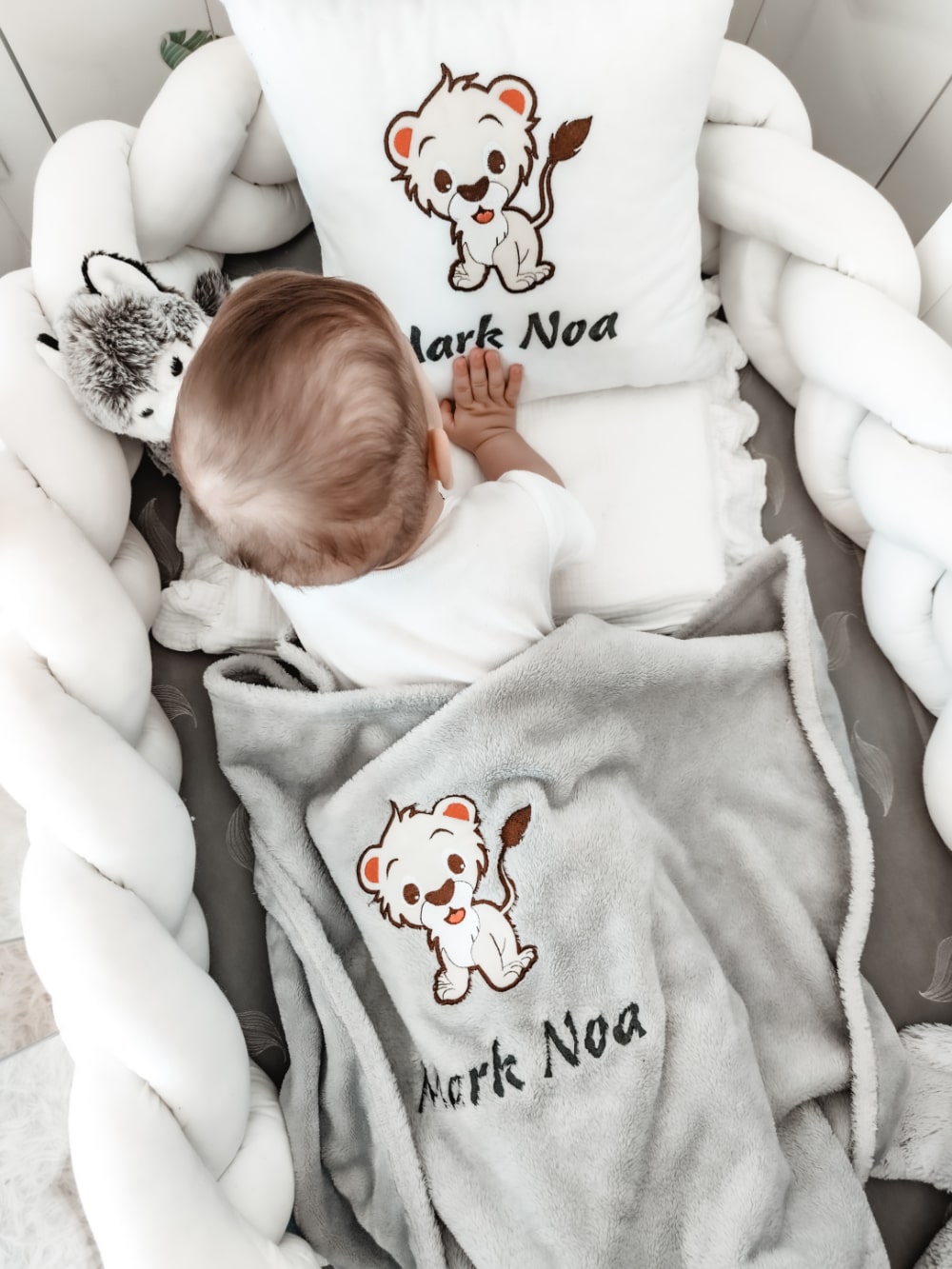 Ljubki dojenček mirno počiva na svoji posteljici in se stiska ob mehko in udobno prilagojeno blazino in odejo, ki sta prilagojeni z njegovim imenom in očarljivim dizajnom.