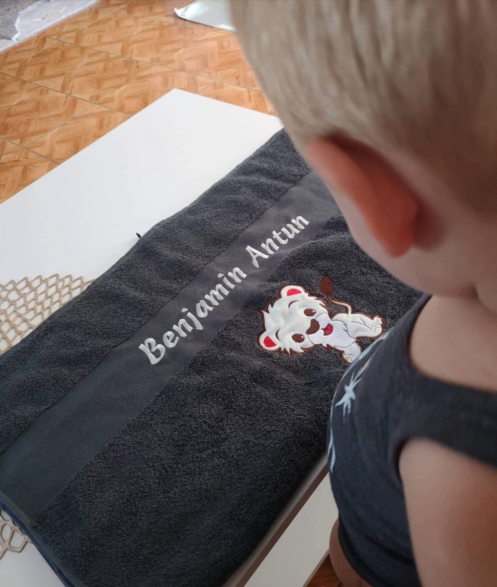 Fant s ponosom razkazuje svojo prilagojeno brisačo z živahnim vzorcem in svojim imenom na njej.