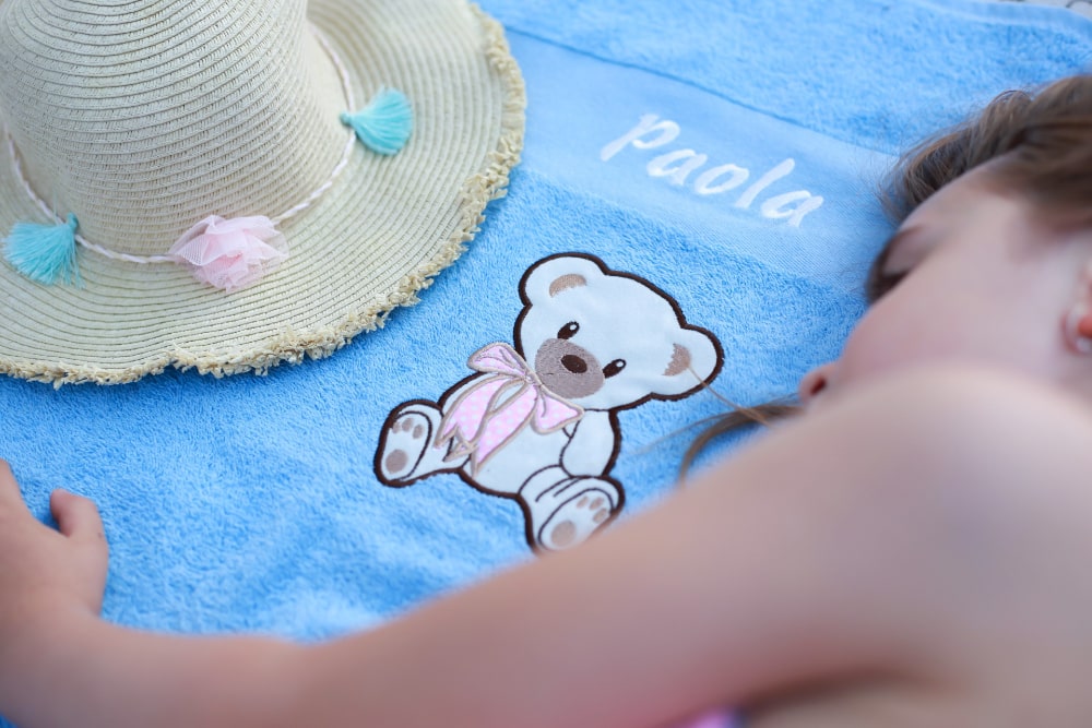 Majhno deklico s ponosom razkazuje svojo prilagojeno brisačo z živahnim vzorcem in svojim imenom na njej.