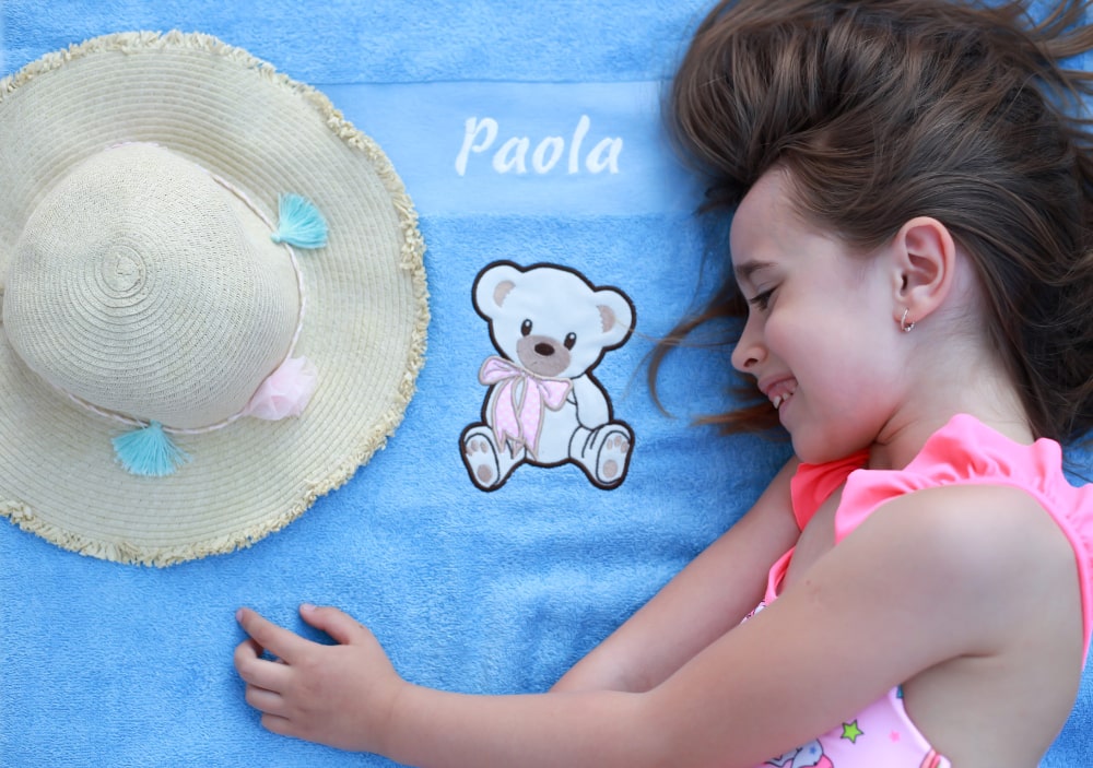 Majhno deklico s ponosom razkazuje svojo prilagojeno brisačo z živahnim vzorcem in svojim imenom na njej.